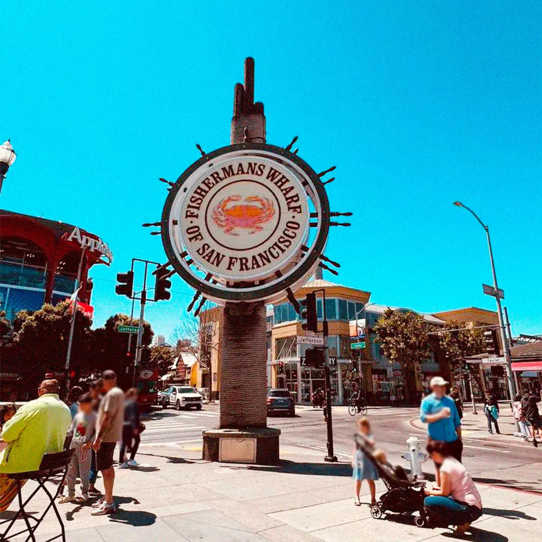 a sign on a pole with Fisherman's Wharf in the background