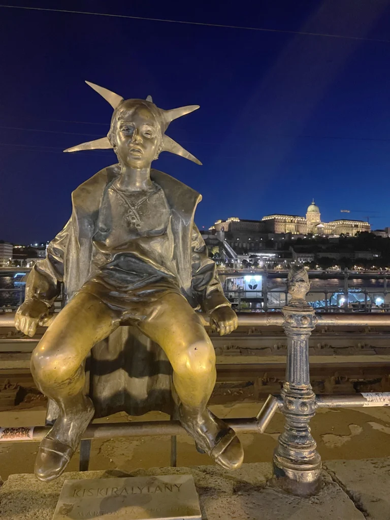 The Little Princess statue on Budapest's Danube promenade with Buda Castle in the background 